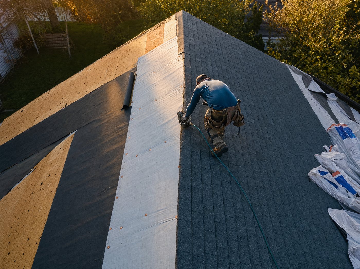 Roof mid tear-off with new underlayment and fresh charcoal shingles being nailed